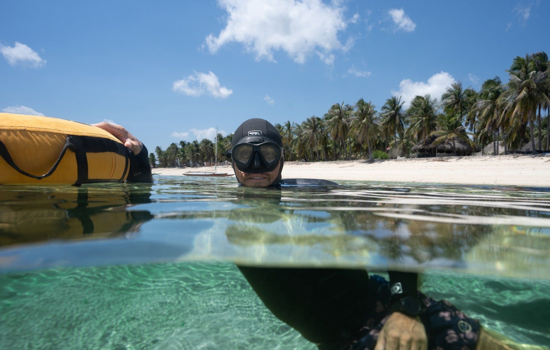 A freediver at the surface in the shallows off Nemberala beach, palms behind